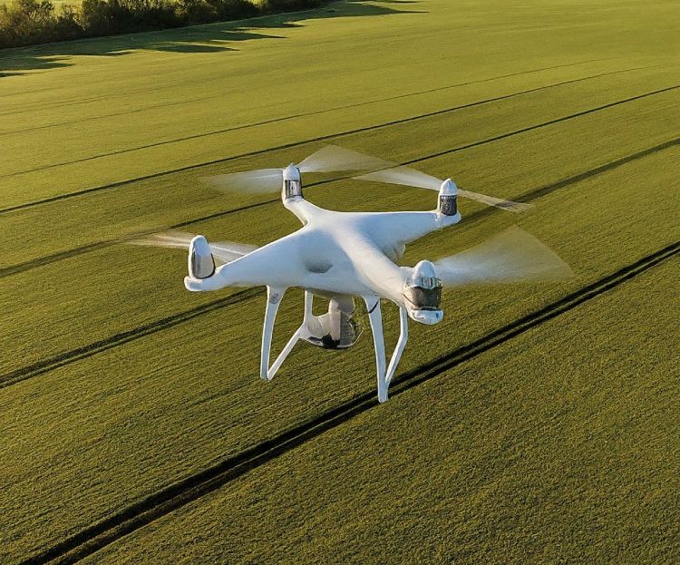 A white quadcopter drone flying over green farmland for surveying purposes