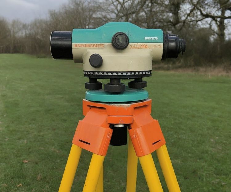 A surveyor's level equipment mounted on a bright yellow tripod in an open field