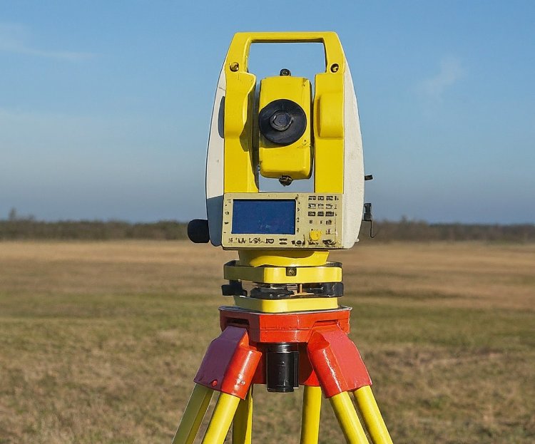 Yellow theodolite survey instrument mounted on a colorful tripod in an open field